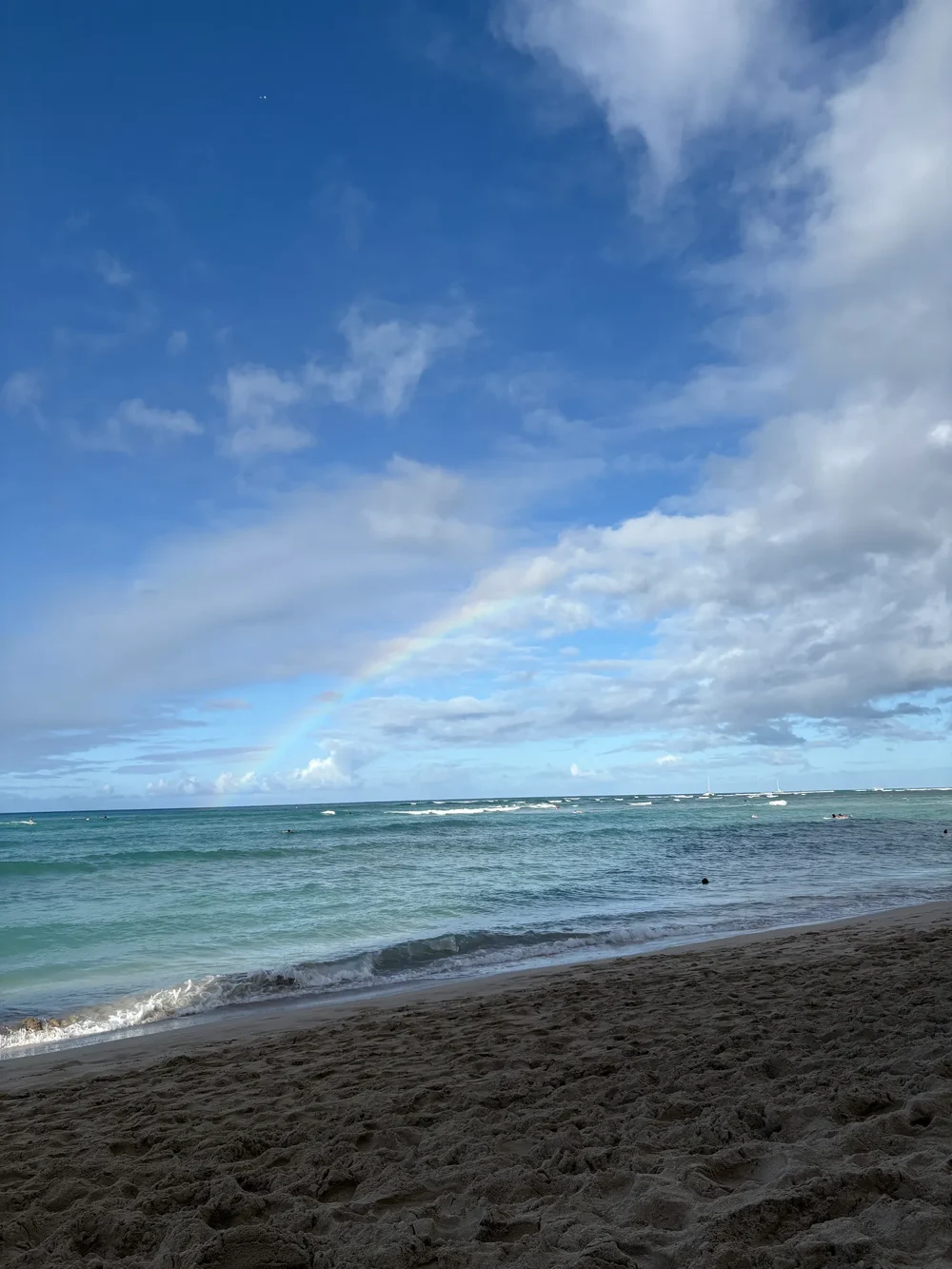 The full rainbow view above the ocean and beach in Hawaiʻi
