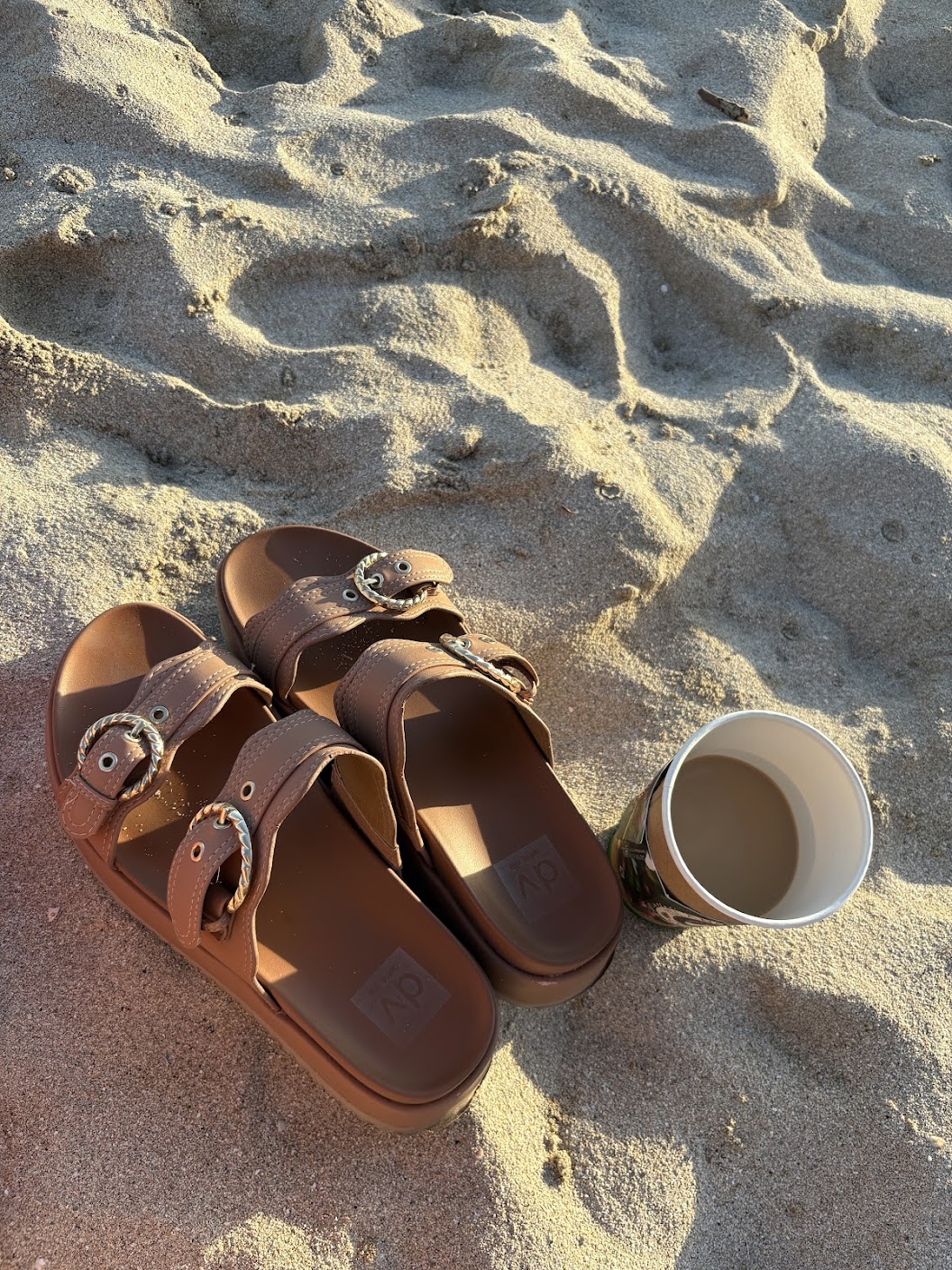 Sandals and a cup resting on sunlit beach sand