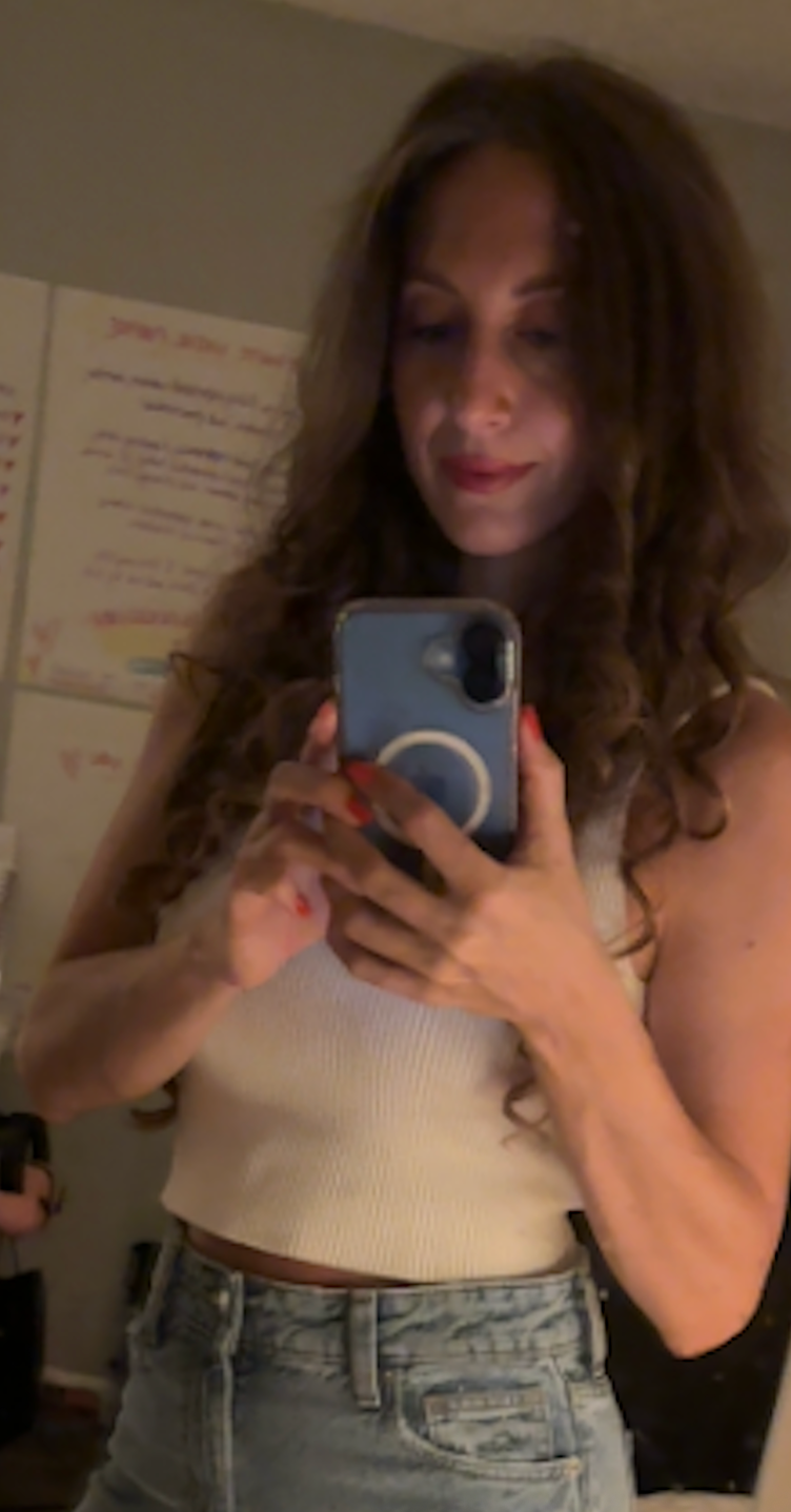 Malana in a cream top and jeans, taking a mirror photo